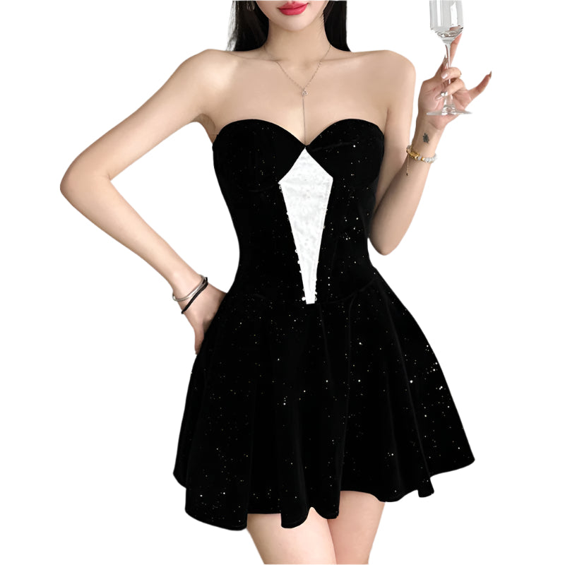 Woman wearing a black strapless dress holding a glass against a plain background